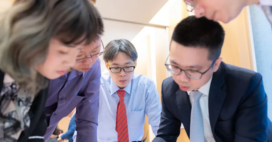 四位學員俯身圍在桌前,神情專注地看著桌上的資料。